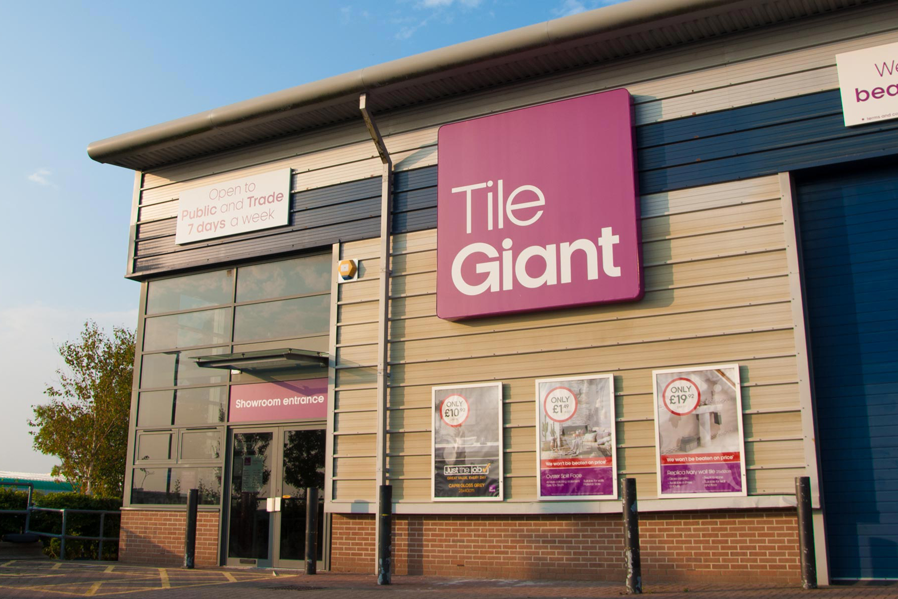 The exterior of a "Tile Giant" retail store with a large pink sign, featuring posters advertising products.