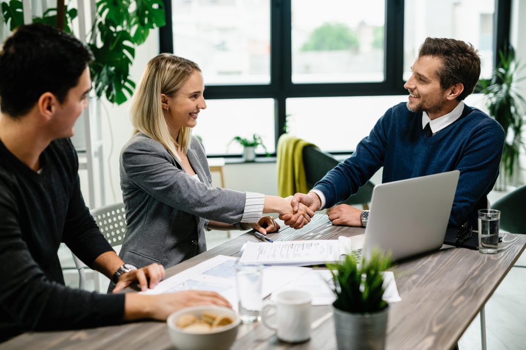 A young, happy couple meeting with financial advisor and the woman shakes hands with advisor